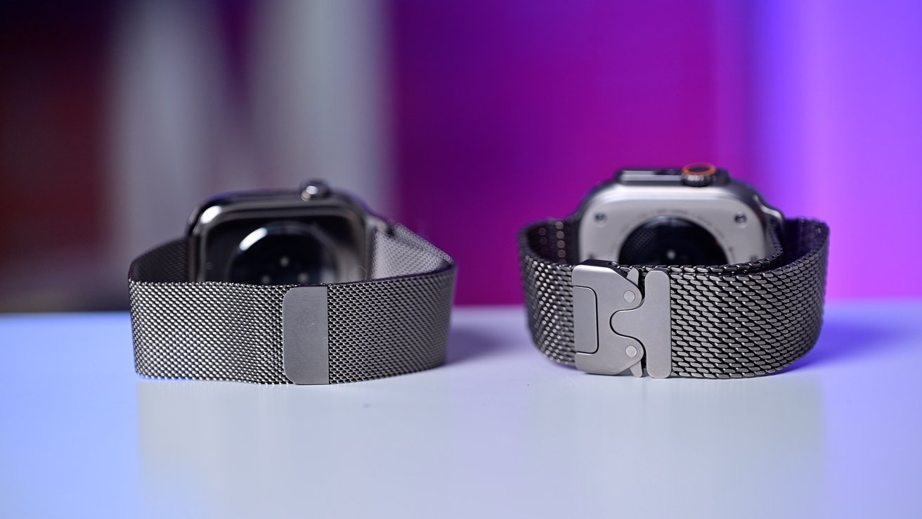 Two smartwatches with metallic mesh bands are displayed on a surface, set against a blurred pink and purple background.