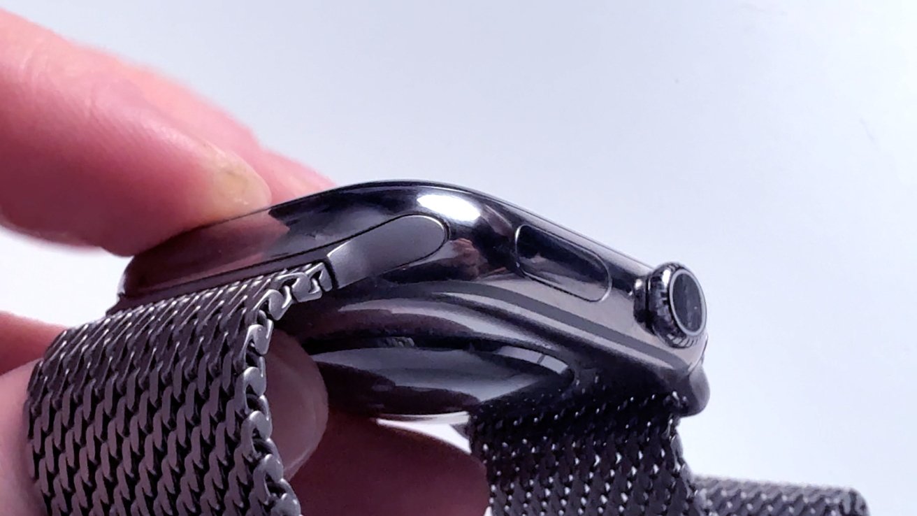 Close-up of a hand holding a smartwatch with a metal mesh band, side view showing the digital crown and button.
