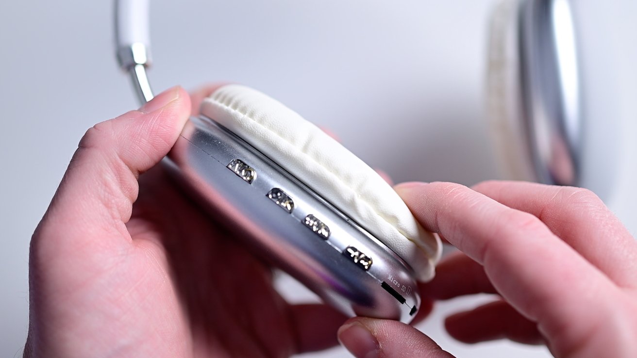 Hands holding white over-ear headphones, focusing on ear pad and ports.