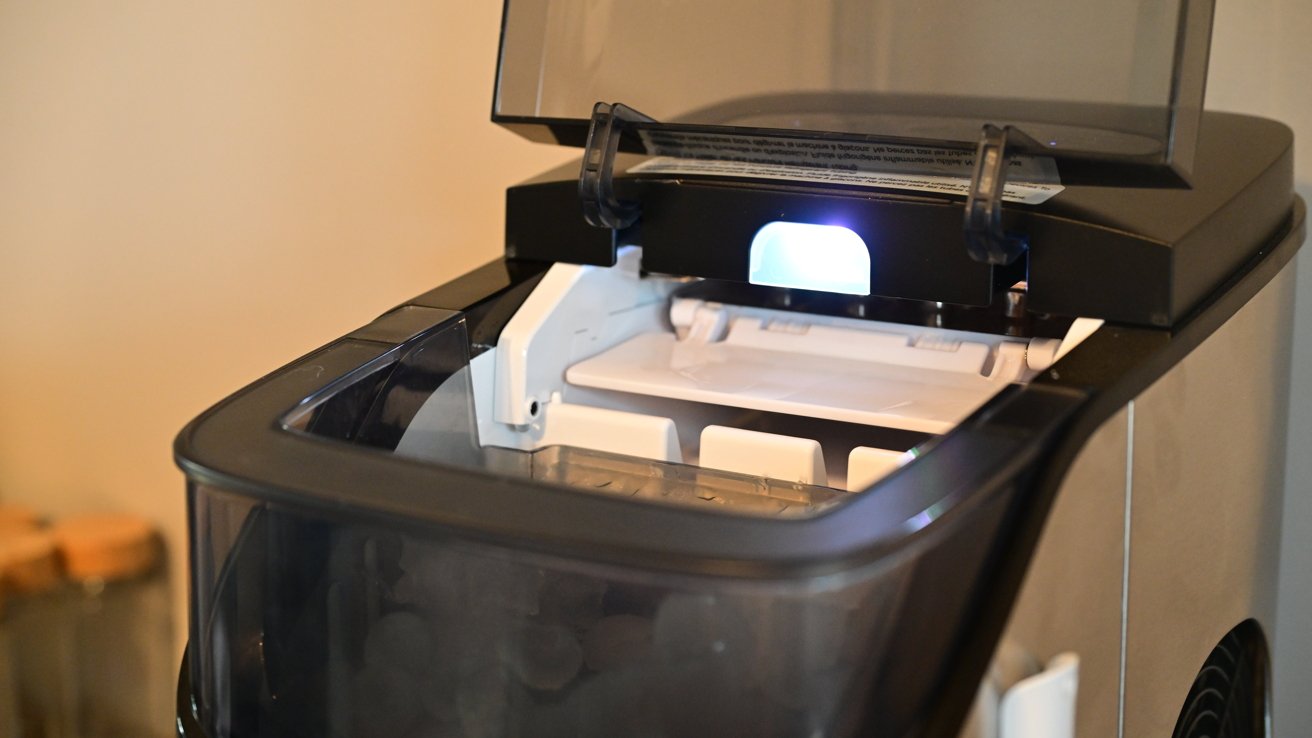 The top of an ice maker with the hood open, showing the ice inside behind a frosted front
