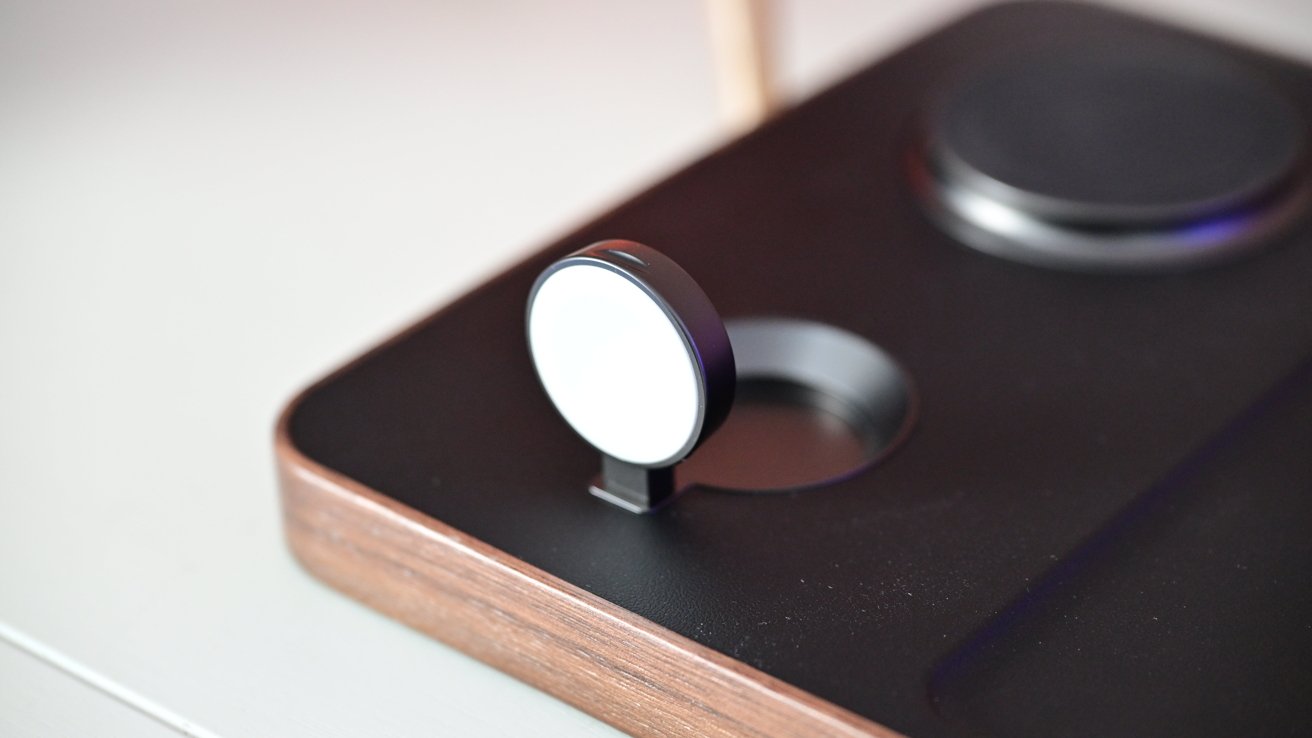 A close-up of a sleek black and wood wireless charging station with a circular charging pad and an adjustable magnetic mount.